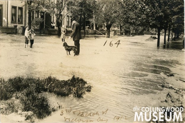 A sepia tone photo on a man, a dog and some children standing in a flooded street.