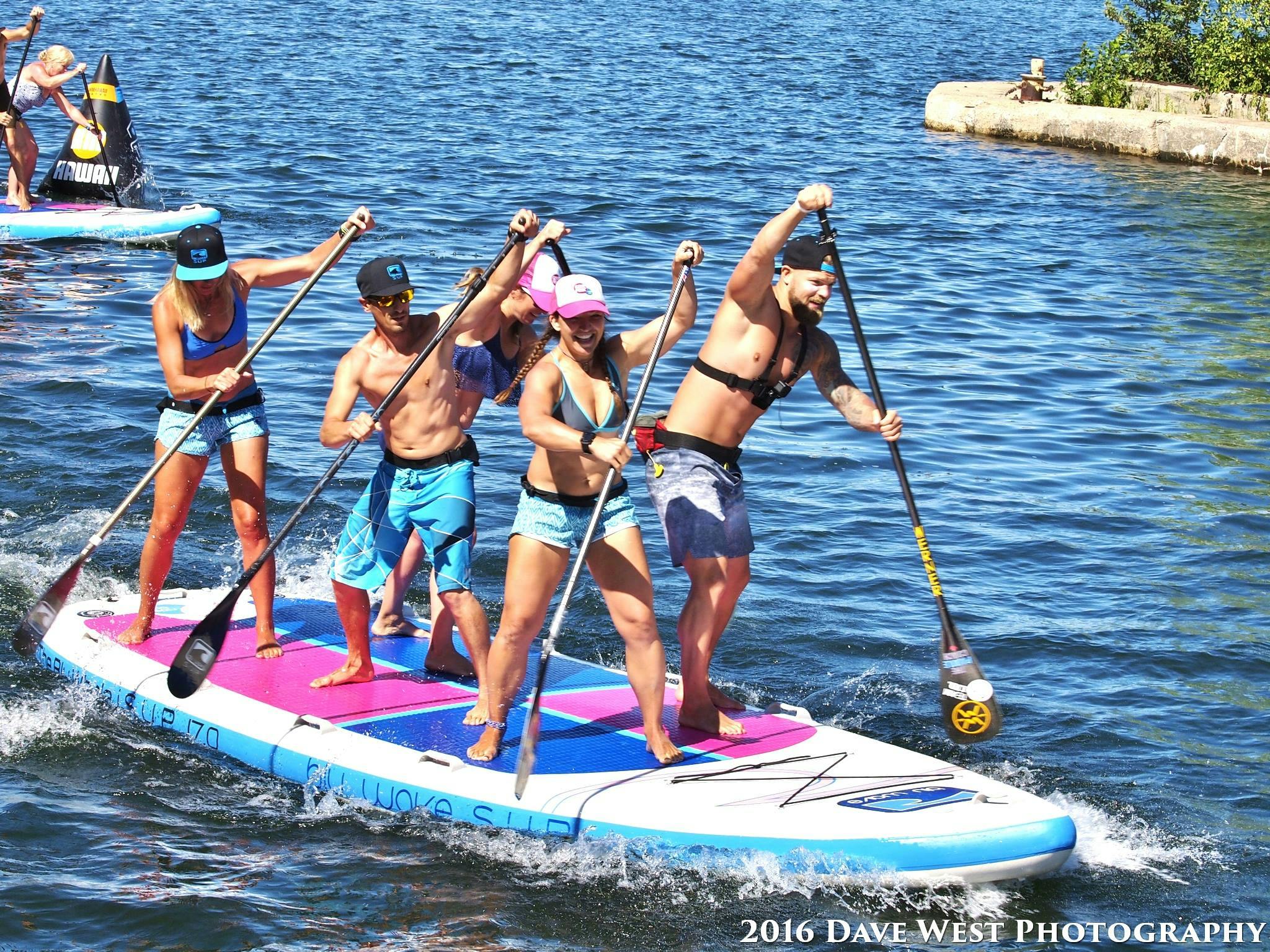 5 adults standing and paddling a large paddle board. 