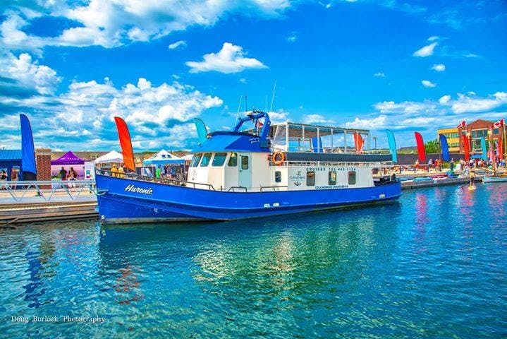 A blue boat docked near the waterfront where people are paddle boarding. 