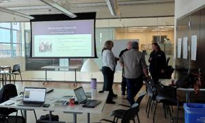 Image of 5 individuals standing in a circle talking beside a screen that reads Climate Impact Statements
