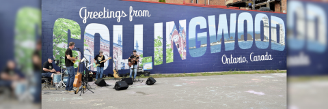 A band plays infront of a postcard style mural